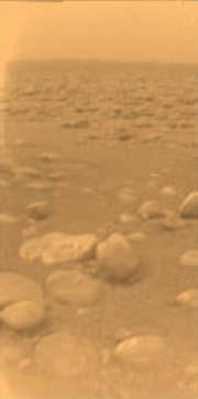 Huygens has found a hydrocarbon beach on Titan. The flat boulder in the middle of the picture is about 15 centimetres across, and lies about 85 centimetres away from the probe. The image has been tinted orange to represent the approximate colour of Titan'