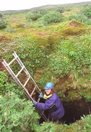 The cave opens to a simple hole in the tundra, which Kristine Crossen descends by ladder