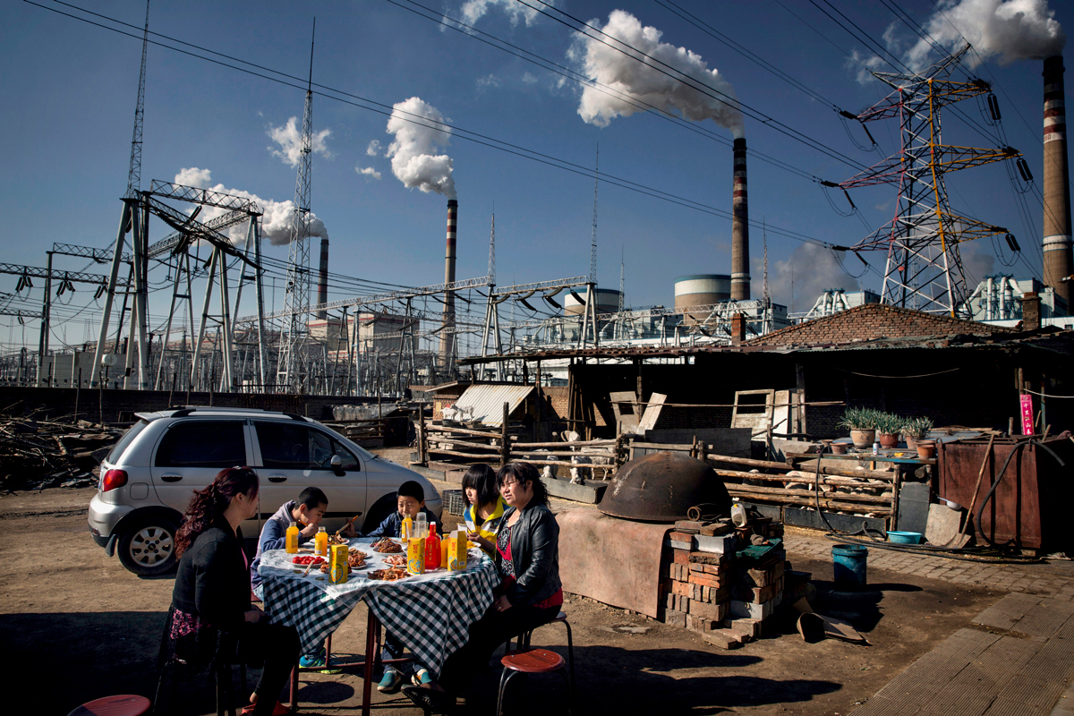 A family eats a meal beneath the smoke stacks and pylons of the Datong No. 2 coal fired power plant.