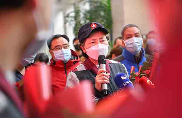 Li Lanjuan wearing a white face mask and baseball cap speaking to a crowd through a microphone.