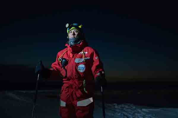 Verena Mohaupt photographed wearing red cold weather gear, skis and holding ski poles on an ice floe during Arctic night.