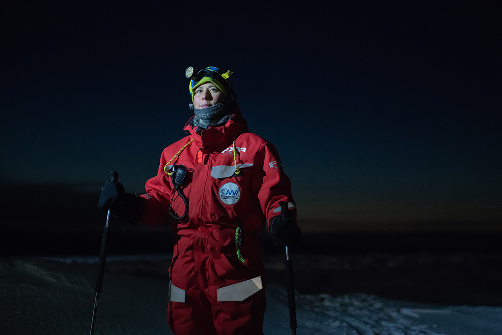 Verena Mohaupt photographed wearing red cold weather                gear, skis and holding ski poles on an ice floe during                Arctic night.
