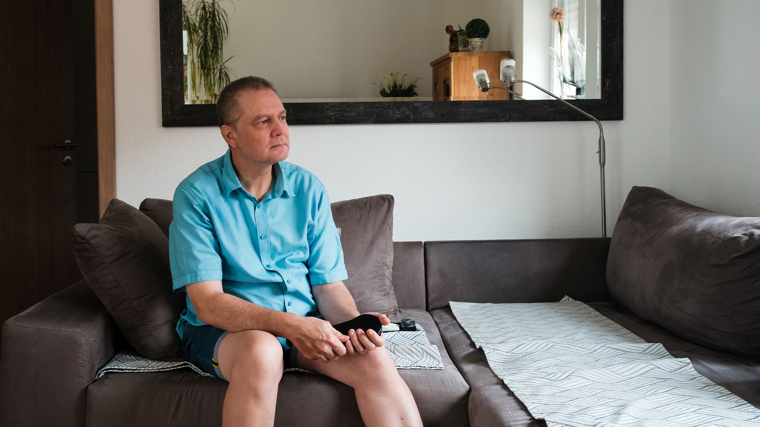 Markus Bohle holds his device while sitting on his sofa at home.