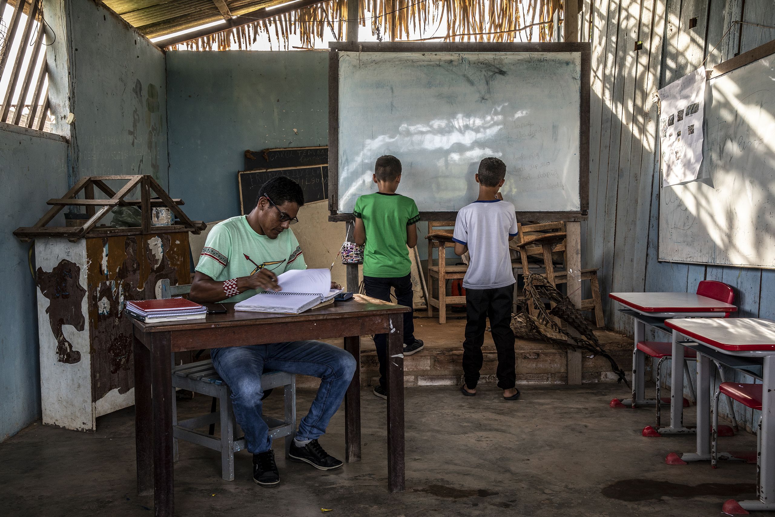 Munduruku teacher looks at his students homework as they take notes in the board on a decaying  rural school in Santarem, northern Para state in Brazil, May 8, 2023.