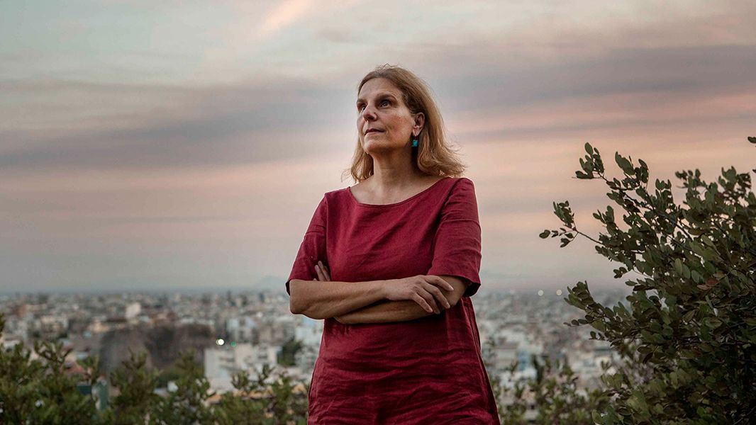 Portrait of Eleni Myrivili wearing a red dress standing on a hillside above Athens.