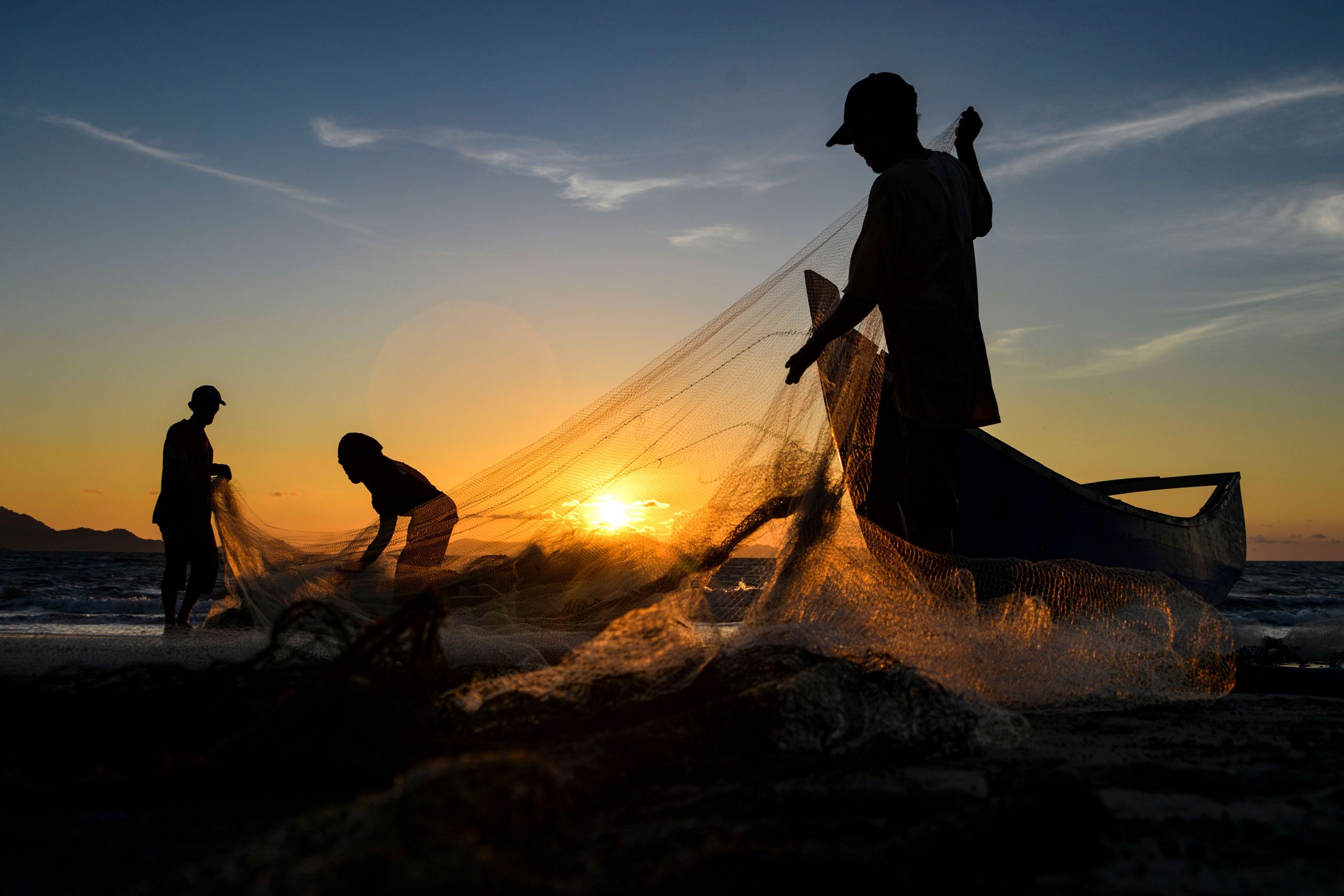 Silhouettes of fishermen cleaning their nets at sunset