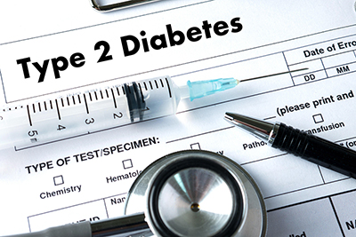 一张剪贴板的照片，上面有一张名为“2 型糖尿病”的医学实验室测试表。 一个注射器、一支笔和一个听诊器横在上面。