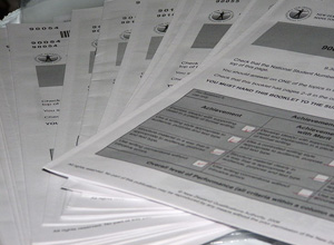 A black-and-white photograph shows a pile of paper applications fanned out across a flat surface.